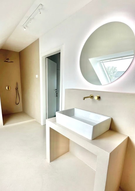 Helles, modernes Badezimmer mit beiger Betonoptik und goldfarbenen Armaturen.