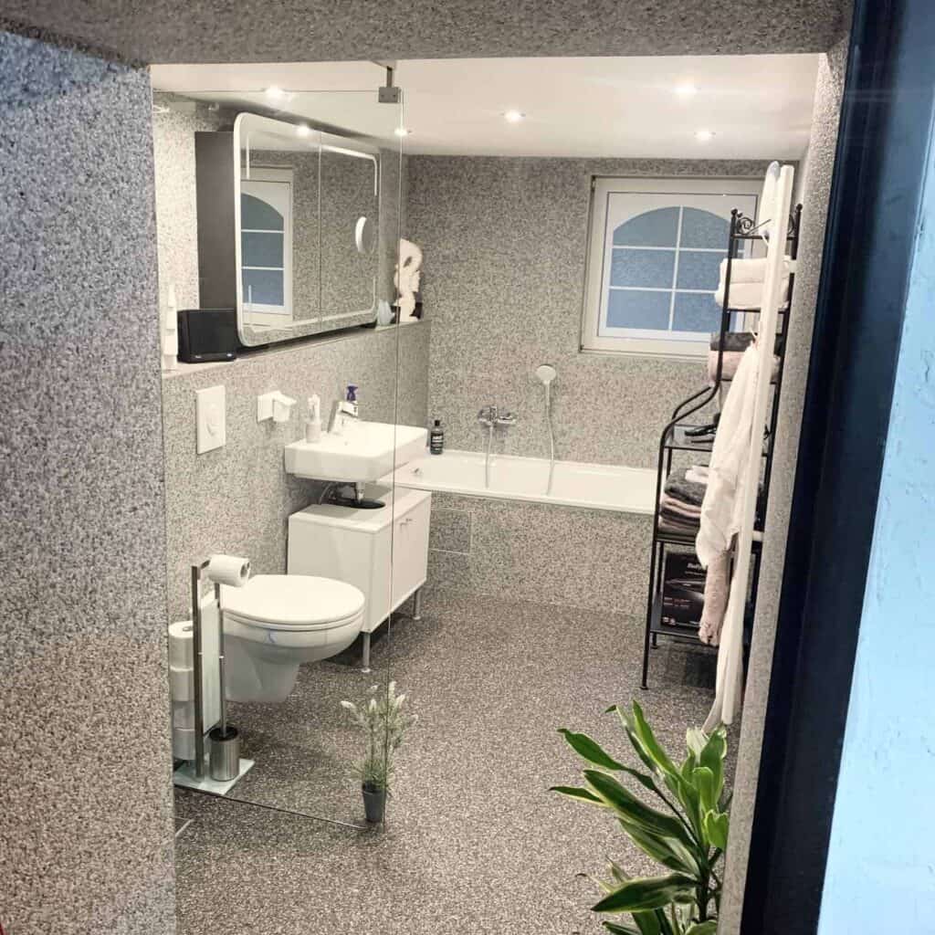 Hellgrauer Steinteppich als Beschichtung für Wand und Boden im Badezimmer.