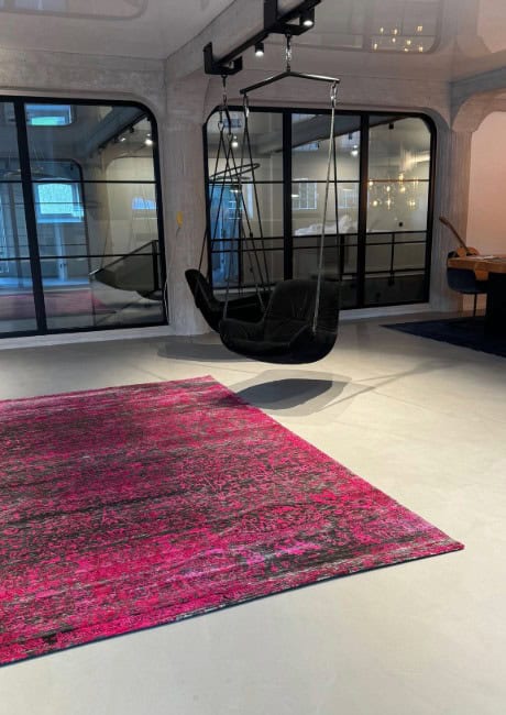 Home 5 Wohnbereich mit hellgrauem Bodenbelag in Betonoptik unter pink-schwarzen Teppich und einer schwarzen Hängeschaukel.