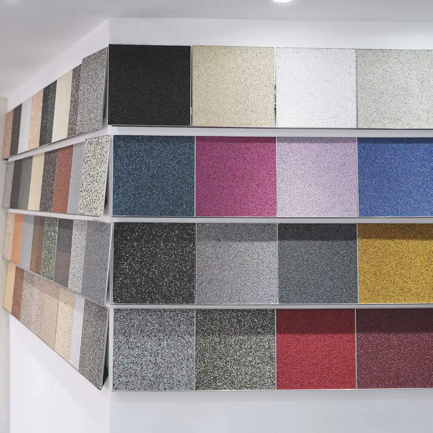 Steinteppich in Bonn: Ausstellung verschiedener Steinteppich-Musterplatten in zahlreichen Farben und Oberflächenstrukturen, darunter Grau, Beige, Anthrazit, Blau, Rot und Pink.
